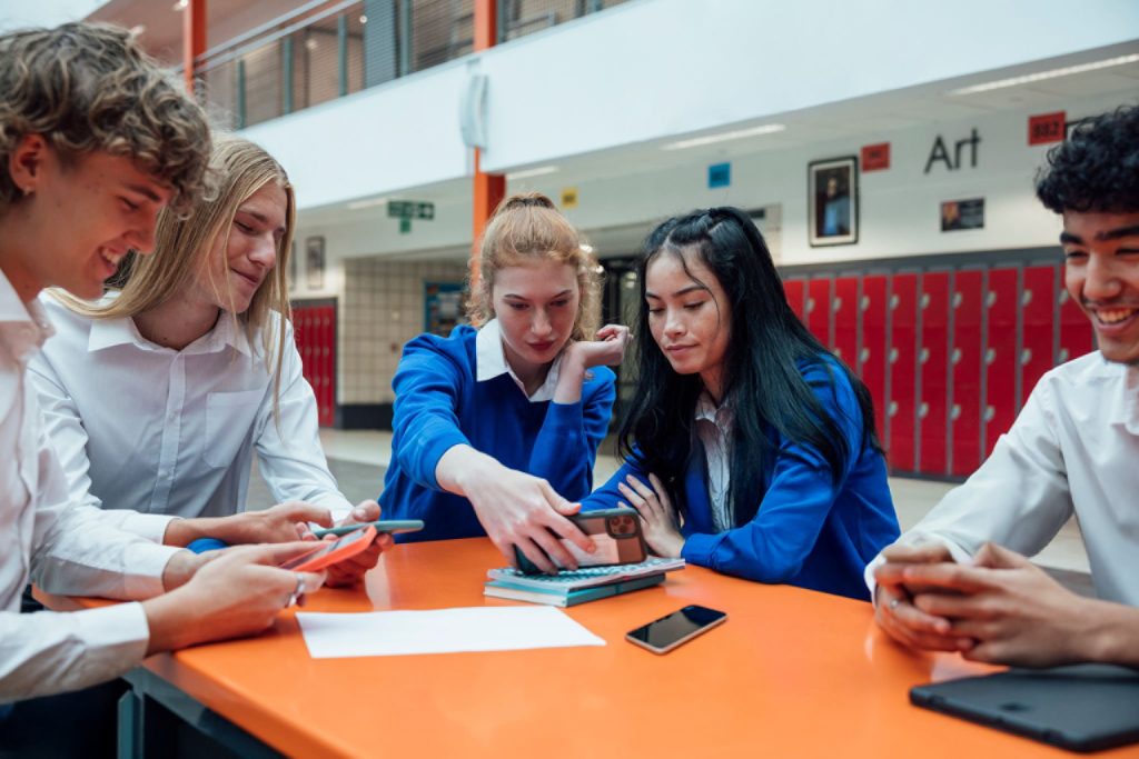 School Kids On Phones Around Table